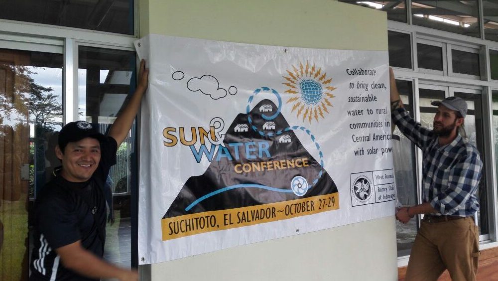 Two people display a banner that advertises a water conference.